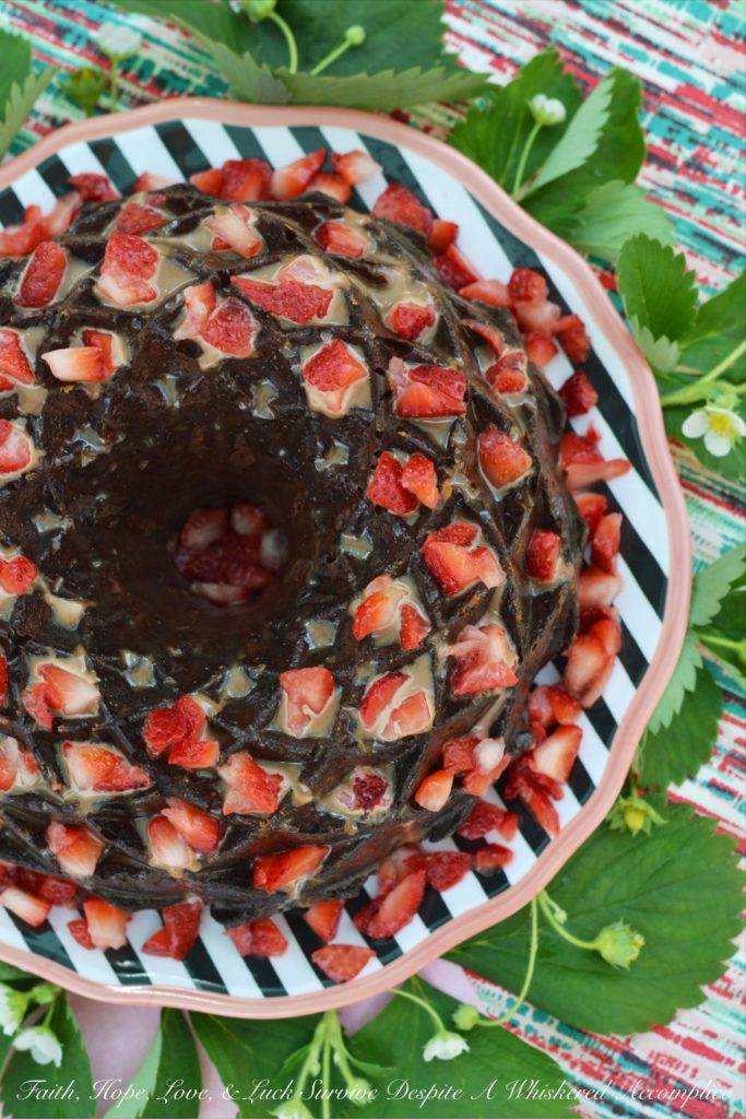 A delicate strawberry Bundt cake, poked and filled with strawberry purée, covered in chocolate sauce, and then garnished with even more fresh strawberries.