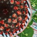 A delicate strawberry Bundt cake, poked and filled with strawberry purée, covered in chocolate sauce, and then garnished with even more fresh strawberries.