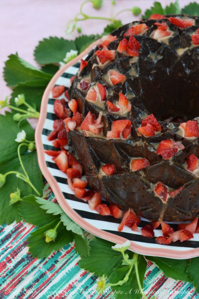 A delicate strawberry Bundt cake, poked and filled with strawberry purée, covered in chocolate sauce, and then garnished with even more fresh strawberries.