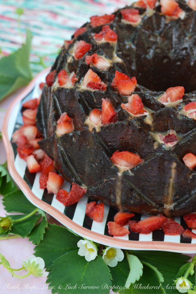 A delicate strawberry Bundt cake, poked and filled with strawberry purée, covered in chocolate sauce, and then garnished with even more fresh strawberries.