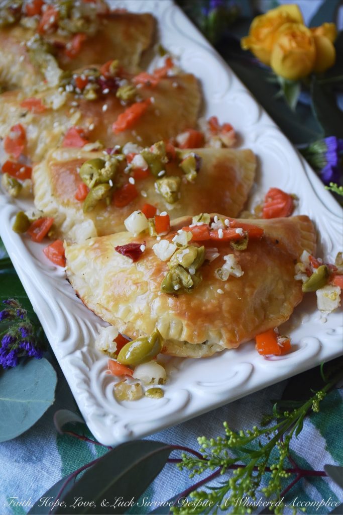 Oven-Baked Mardi Gras Muffuletta Empanadas - Looking to celebrate Mardi Gras with a unique and festive appetizer? Then these oven-baked muffuletta empanadas are just what you're looking for. Each empanada is stuffed with capicola, mortadella, salami, provolone cheese, and just the tiniest bit of Italian olive spread. After they are baked to golden brown perfection, you simply serve them topped with additional Italian olive spread and a light sprinkling of sesame seeds.