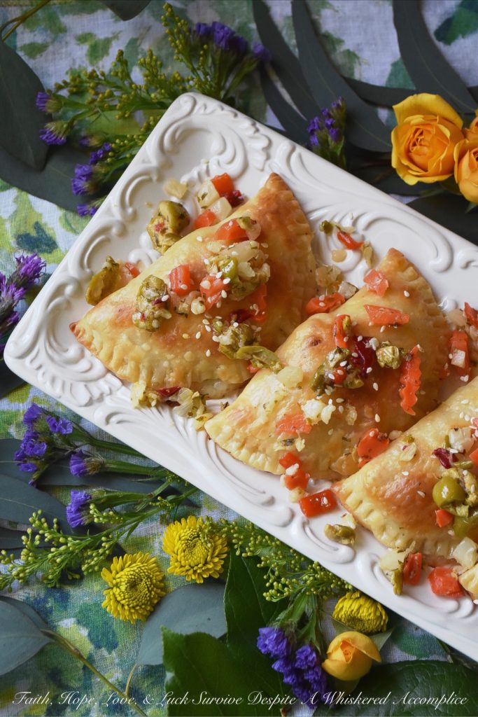 Oven-Baked Mardi Gras Muffuletta Empanadas - Looking to celebrate Mardi Gras with a unique and festive appetizer? Then these oven-baked muffuletta empanadas are just what you're looking for. Each empanada is stuffed with capicola, mortadella, salami, provolone cheese, and just the tiniest bit of Italian olive spread. After they are baked to golden brown perfection, you simply serve them topped with additional Italian olive spread and a light sprinkling of sesame seeds.