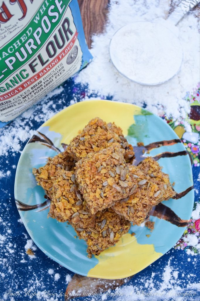 Crunchy Dried Cherry Applesauce Cake Bars - Are you looking for a delicious cakey dessert, filled with dried fruit, that has an amazing crunch? Well then, these applesauce cake bars are just what you're looking for. They're filled with dried cherries and sunflower seeds, which makes this moist and chewy. Then, they're covered in a sweet topping made with brown sugar, butter, sunflower seeds, and crushed corn flakes to make them over-the-top crunchy. These are seriously crunchtastic.