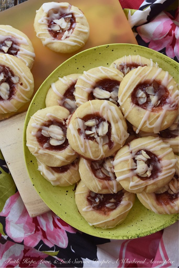 Dark Rum Cherry Almond Thumbprint Cookies - What's better than a Christmas thumbprint cookie? A boozy Christmas thumbprint cookie made using dark rum and cherry preserves. Add on a drizzle of powdered sugar rum glaze and a few sliced almonds, and these boozy Christmas cookies will certainly grab your attention with their festive presentation if not their amazing and absolutely delicious taste.