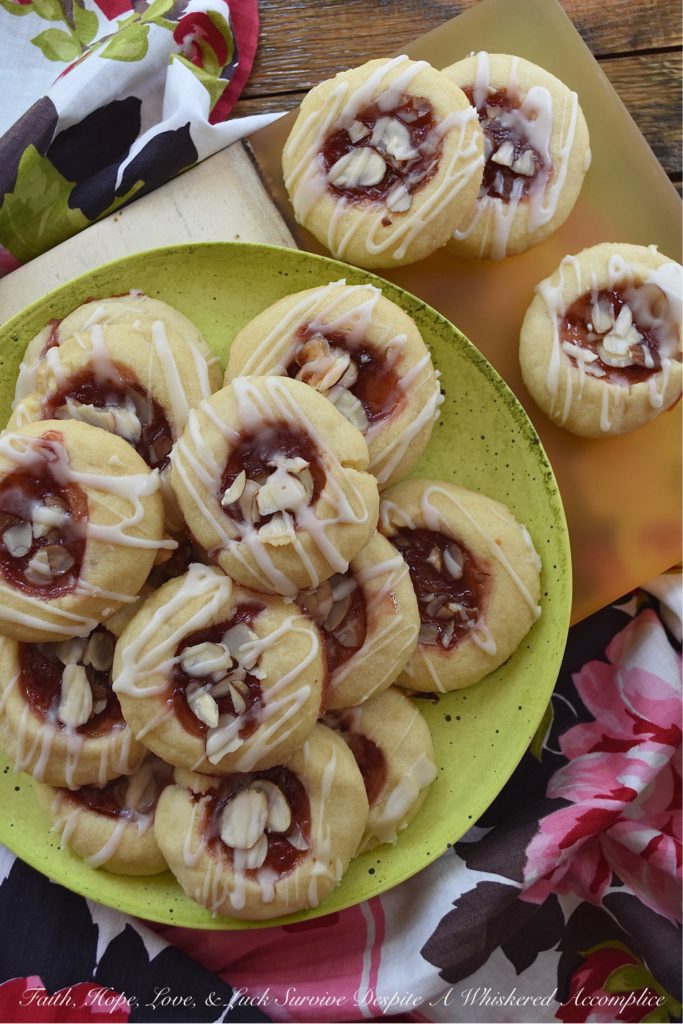 Dark Rum Cherry Almond Thumbprint Cookies - What's better than a Christmas thumbprint cookie? A boozy Christmas thumbprint cookie made using dark rum and cherry preserves. Add on a drizzle of powdered sugar rum glaze and a few sliced almonds, and these boozy Christmas cookies will certainly grab your attention with their festive presentation if not their amazing and absolutely delicious taste.