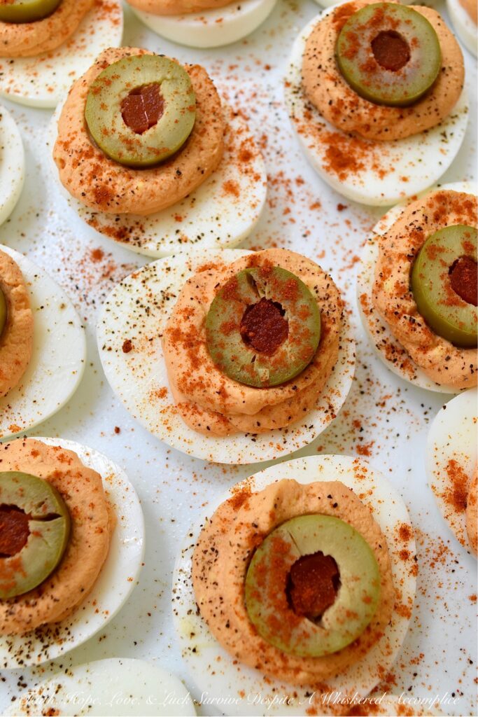 Pimento & Spanish Queen Olive Deviled Eggs - A simple little jar of drained diced pimentos is the secret to these creamy deviled eggs topped with Spanish Queen Olives. They're colorful, flavorful, and a welcome change from most boring deviled egg recipes. With their gorgeous color and mild red pepper flavor, these pimento and green olive deviled eggs are sure to be a hit at your next party or cookout.