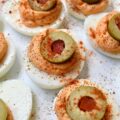Pimento & Spanish Queen Olive Deviled Eggs - A simple little jar of drained diced pimentos is the secret to these creamy deviled eggs topped with Spanish Queen Olives. They're colorful, flavorful, and a welcome change from most boring deviled egg recipes. With their gorgeous color and mild red pepper flavor, these pimento and green olive deviled eggs are sure to be a hit at your next party or cookout.