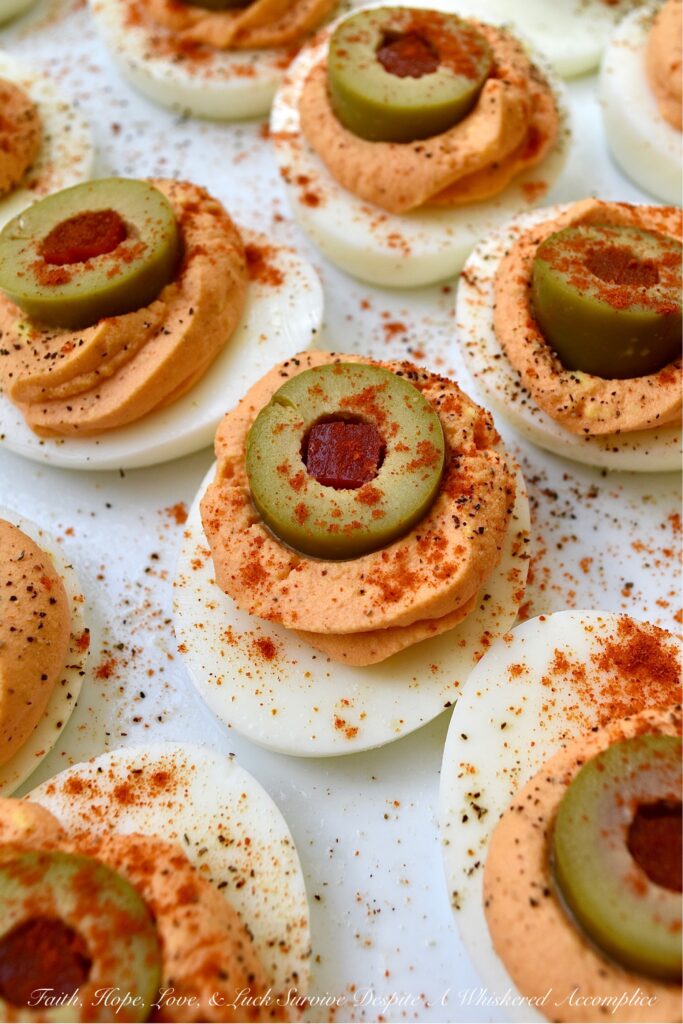 Pimento & Spanish Queen Olive Deviled Eggs - A simple little jar of drained diced pimentos is the secret to these creamy deviled eggs topped with Spanish Queen Olives. They're colorful, flavorful, and a welcome change from most boring deviled egg recipes. With their gorgeous color and mild red pepper flavor, these pimento and green olive deviled eggs are sure to be a hit at your next party or cookout.