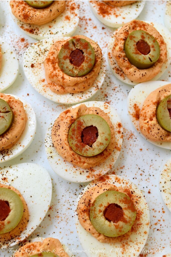 Pimento & Spanish Queen Olive Deviled Eggs - A simple little jar of drained diced pimentos is the secret to these creamy deviled eggs topped with Spanish Queen Olives. They're colorful, flavorful, and a welcome change from most boring deviled egg recipes. With their gorgeous color and mild red pepper flavor, these pimento and green olive deviled eggs are sure to be a hit at your next party or cookout.