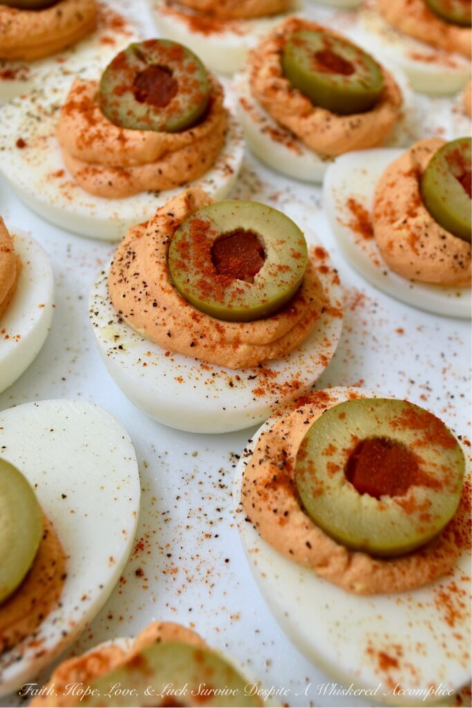 Pimento & Spanish Queen Olive Deviled Eggs - A simple little jar of drained diced pimentos is the secret to these creamy deviled eggs topped with Spanish Queen Olives. They're colorful, flavorful, and a welcome change from most boring deviled egg recipes. With their gorgeous color and mild red pepper flavor, these pimento and green olive deviled eggs are sure to be a hit at your next party or cookout.