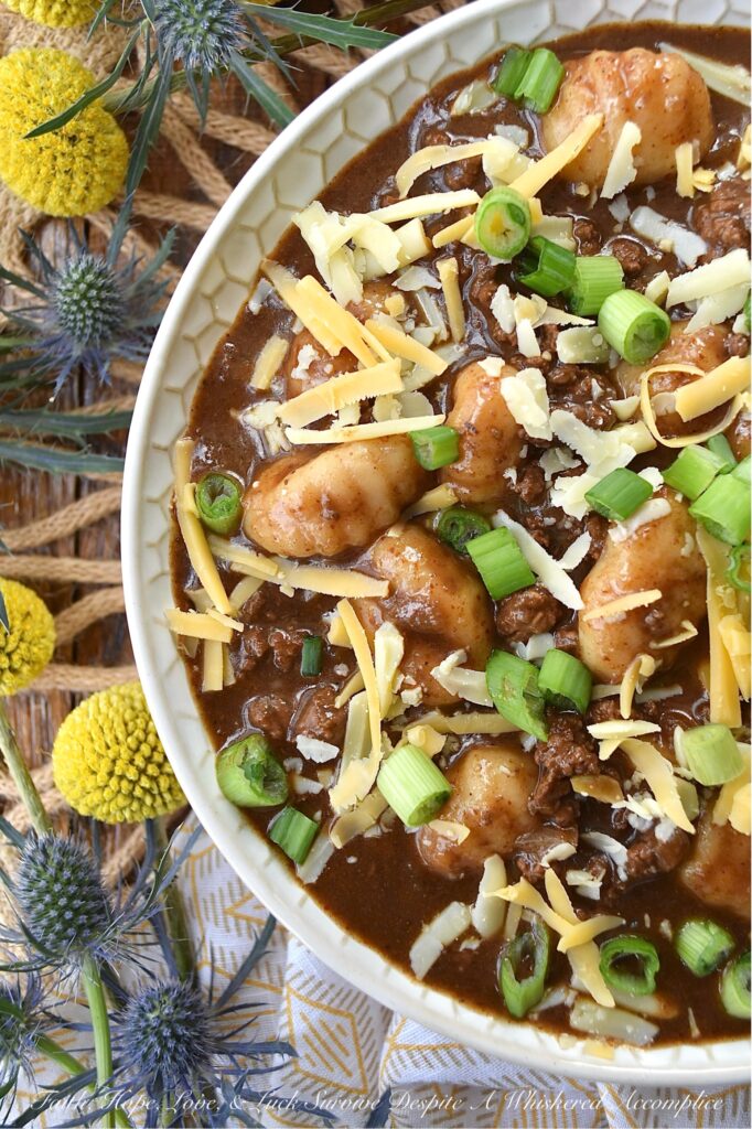 Guinness Stew Cincinnati Chili with Gnocchi - This hearty and flavorful one-pot stew and chili mash-up combines the bold flavors of Guinness stew and Cincinnati chili while taking things to the next level with the addition of potato gnocchi and a garnish of freshly shredded cheddar cheese and finely chopped scallions. Packed with spices and a perfect balance of sweetness and heat, this dish is sure to become a new favorite. And, since the gnocchi get even more soft and pillowy as the Guinness Stew Cincinnati Chili with Gnocchi rests overnight in the fridge, this is the perfect meal to make ahead and serve on a busy weeknight.