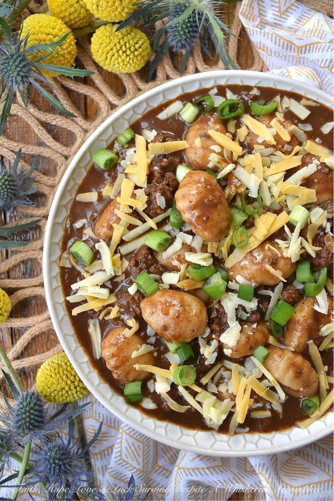 Guinness Stew Cincinnati Chili with Gnocchi - This hearty and flavorful one-pot stew and chili mash-up combines the bold flavors of Guinness stew and Cincinnati chili while taking things to the next level with the addition of potato gnocchi and a garnish of freshly shredded cheddar cheese and finely chopped scallions. Packed with spices and a perfect balance of sweetness and heat, this dish is sure to become a new favorite. And, since the gnocchi get even more soft and pillowy as the Guinness Stew Cincinnati Chili with Gnocchi rests overnight in the fridge, this is the perfect meal to make ahead and serve on a busy weeknight.