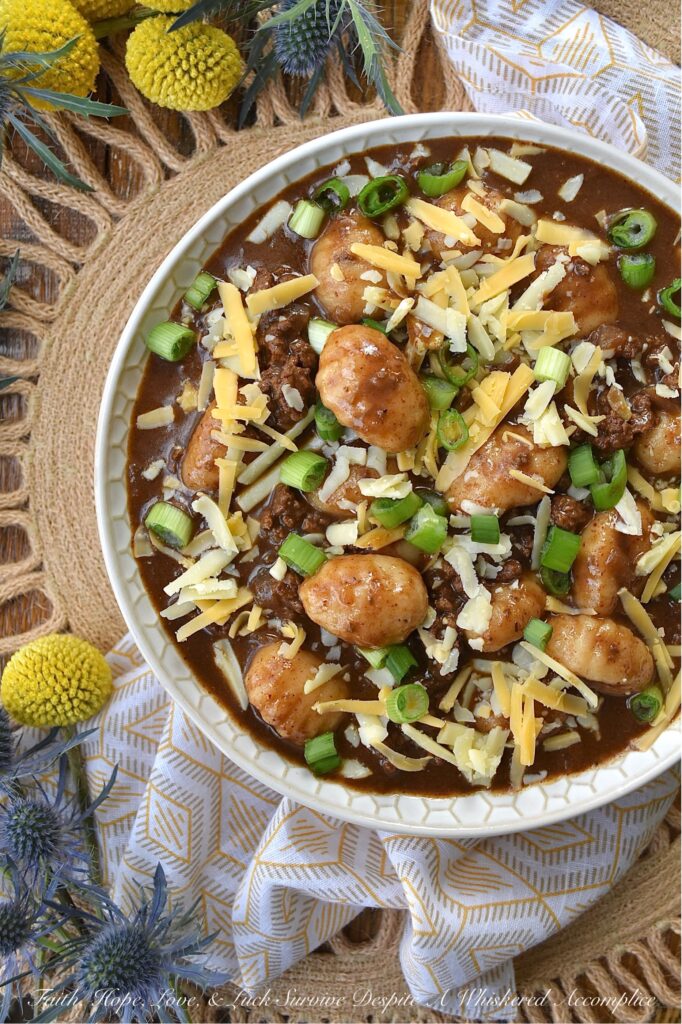 Guinness Stew Cincinnati Chili with Gnocchi - This hearty and flavorful one-pot stew and chili mash-up combines the bold flavors of Guinness stew and Cincinnati chili while taking things to the next level with the addition of potato gnocchi and a garnish of freshly shredded cheddar cheese and finely chopped scallions. Packed with spices and a perfect balance of sweetness and heat, this dish is sure to become a new favorite. And, since the gnocchi get even more soft and pillowy as the Guinness Stew Cincinnati Chili with Gnocchi rests overnight in the fridge, this is the perfect meal to make ahead and serve on a busy weeknight.