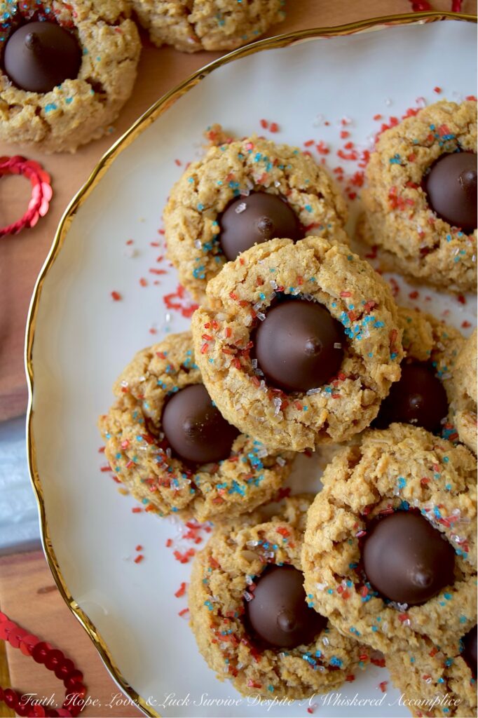 Firecracker Oatmeal Peanut Butter Blossoms - With their combination of creamy peanut butter and chocolatey Hershey's Kisses, these patriotic oatmeal peanut butter blossoms will almost surely cause a summer flavor explosion. These delightful blossom cookies are adorned with a festive and vibrant firecracker-inspired sprinkle of decorative red, white, and blue sugar, making them the perfect addition to any mid-summer celebration or 4th of July gathering.