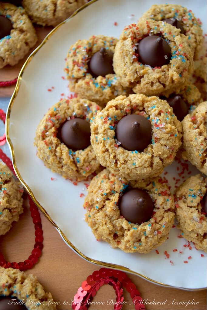 Firecracker Oatmeal Peanut Butter Blossoms - With their combination of creamy peanut butter and chocolatey Hershey's Kisses, these patriotic oatmeal peanut butter blossoms will almost surely cause a summer flavor explosion. These delightful blossom cookies are adorned with a festive and vibrant firecracker-inspired sprinkle of decorative red, white, and blue sugar, making them the perfect addition to any mid-summer celebration or 4th of July gathering.