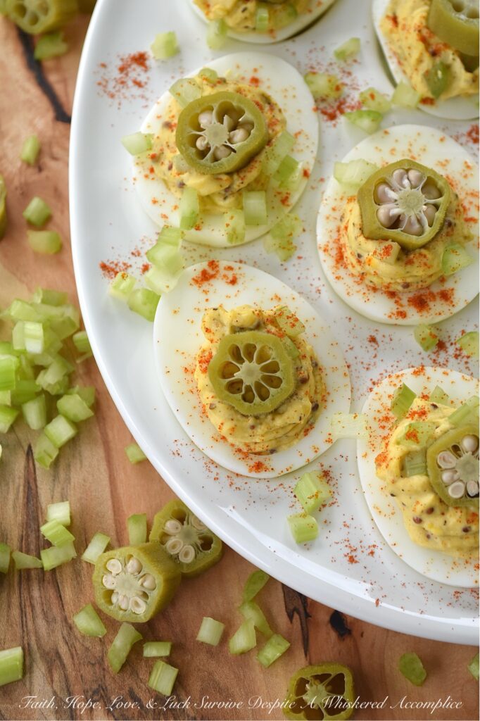 Cajun Deviled Eggs Garnished with Pickled Okra - These Cajun deviled eggs are anything but ordinary. Imagine a creamy, tangy deviled egg filling, kicked up a notch with the vibrant flavors of Cajun seasoning, whole-grain mustard, black pepper, and just a hint of onion powder. These little bites of heaven are then topped with a sprinkle of paprika, a touch of finely chopped celery, and a tangy slice of pickled okra for the ultimate Southern flair. Whether you're celebrating Mardi Gras or simply craving a bold and flavorful bite, these Cajun deviled eggs are sure to be a crowd-pleaser.