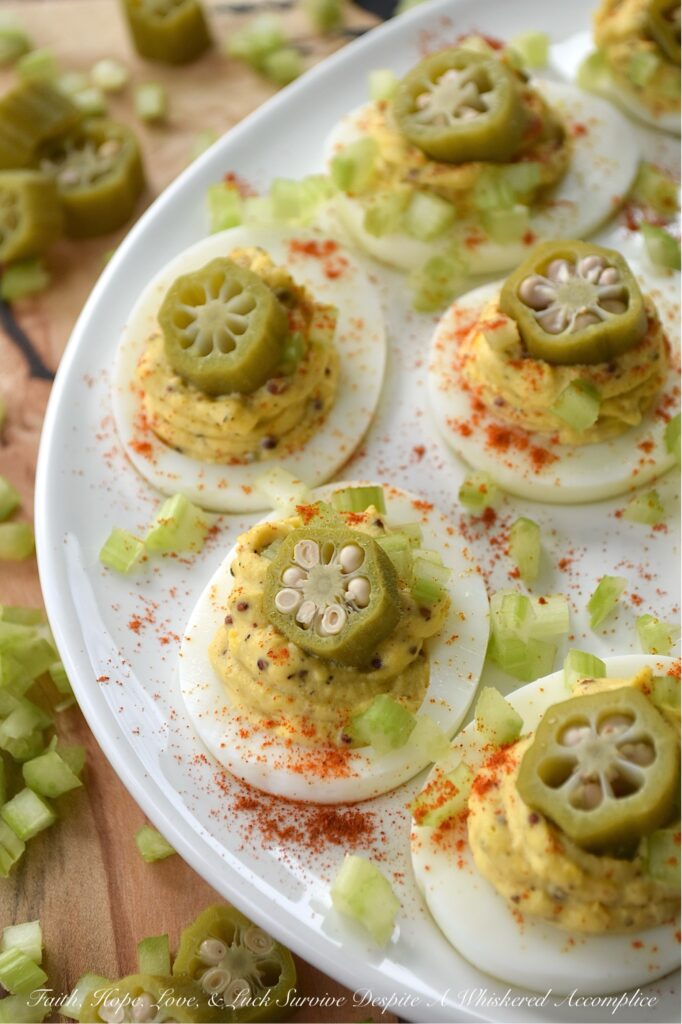 Cajun Deviled Eggs Garnished with Pickled Okra - These Cajun deviled eggs are anything but ordinary. Imagine a creamy, tangy deviled egg filling, kicked up a notch with the vibrant flavors of Cajun seasoning, whole-grain mustard, black pepper, and just a hint of onion powder. These little bites of heaven are then topped with a sprinkle of paprika, a touch of finely chopped celery, and a tangy slice of pickled okra for the ultimate Southern flair. Whether you're celebrating Mardi Gras or simply craving a bold and flavorful bite, these Cajun deviled eggs are sure to be a crowd-pleaser.