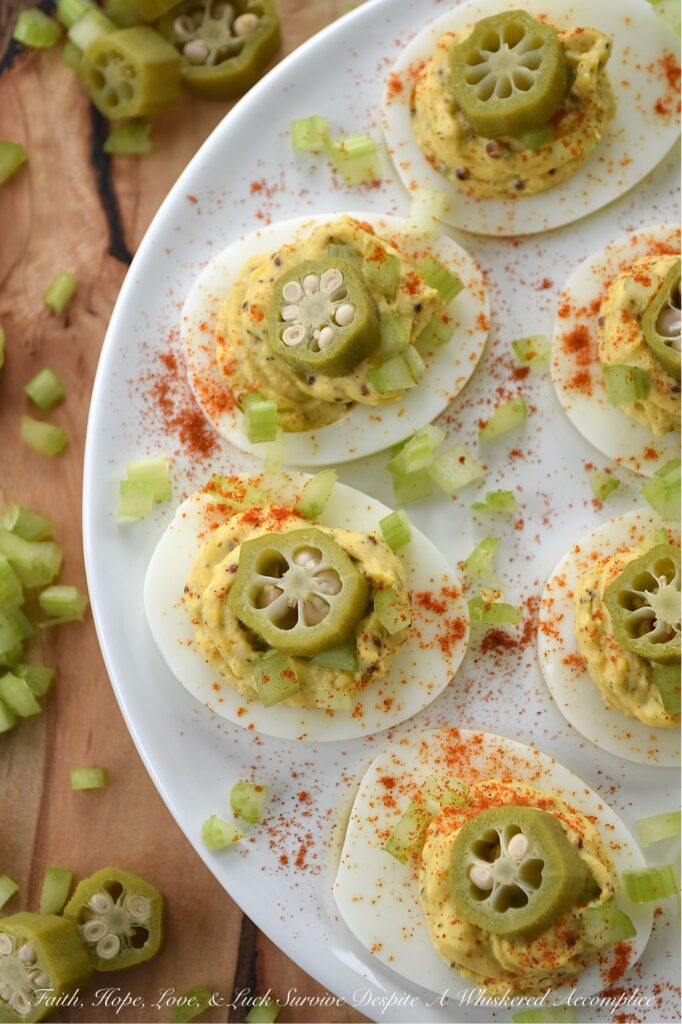Cajun Deviled Eggs Garnished with Pickled Okra - These Cajun deviled eggs are anything but ordinary. Imagine a creamy, tangy deviled egg filling, kicked up a notch with the vibrant flavors of Cajun seasoning, whole-grain mustard, black pepper, and just a hint of onion powder. These little bites of heaven are then topped with a sprinkle of paprika, a touch of finely chopped celery, and a tangy slice of pickled okra for the ultimate Southern flair. Whether you're celebrating Mardi Gras or simply craving a bold and flavorful bite, these Cajun deviled eggs are sure to be a crowd-pleaser.