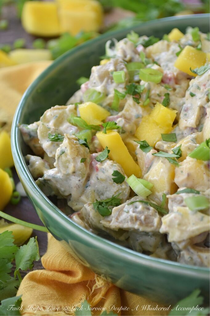 Creamy Cilantro Herb Caribbean Potato Salad - Tired of the same boring traditional potato salad? Bring a little tropical flavor to your next picnic or barbecue with this creamy Caribbean version, featuring jerk seasoning, diced pimentos, and fresh mango. This flavorful herby potato salad has a touch of heat and is just a little bit sweet. With cilantro, scallions, and a splash of vinegar to brighten things up, this island-inspired recipe turns a bag of small yellow potatoes into a side dish that will have everyone practically begging you for the recipe.