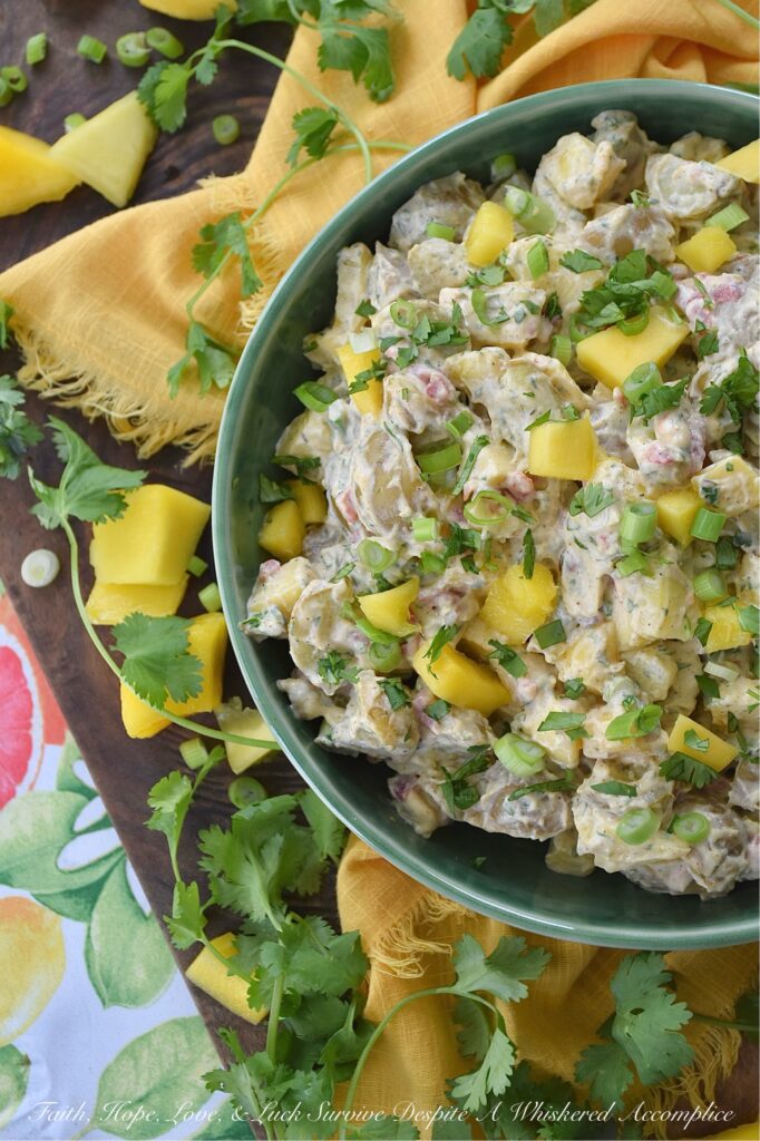 Creamy Cilantro Herb Caribbean Potato Salad - Tired of the same boring traditional potato salad? Bring a little tropical flavor to your next picnic or barbecue with this creamy Caribbean version, featuring jerk seasoning, diced pimentos, and fresh mango. This flavorful herby potato salad has a touch of heat and is just a little bit sweet. With cilantro, scallions, and a splash of vinegar to brighten things up, this island-inspired recipe turns a bag of small yellow potatoes into a side dish that will have everyone practically begging you for the recipe.