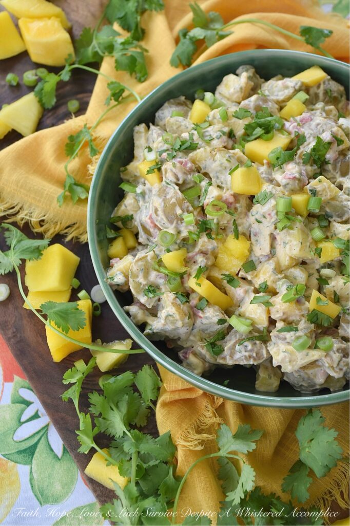 Creamy Cilantro Herb Caribbean Potato Salad - Tired of the same boring traditional potato salad? Bring a little tropical flavor to your next picnic or barbecue with this creamy Caribbean version, featuring jerk seasoning, diced pimentos, and fresh mango. This flavorful herby potato salad has a touch of heat and is just a little bit sweet. With cilantro, scallions, and a splash of vinegar to brighten things up, this island-inspired recipe turns a bag of small yellow potatoes into a side dish that will have everyone practically begging you for the recipe.