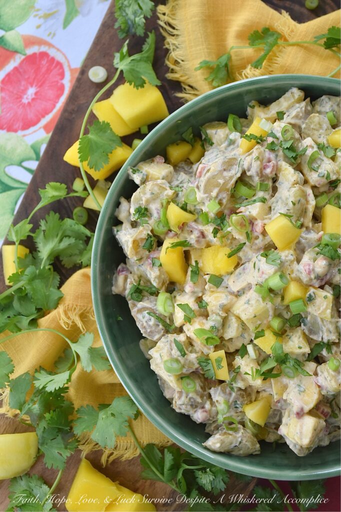 Creamy Cilantro Herb Caribbean Potato Salad - Tired of the same boring traditional potato salad? Bring a little tropical flavor to your next picnic or barbecue with this creamy Caribbean version, featuring jerk seasoning, diced pimentos, and fresh mango. This flavorful herby potato salad has a touch of heat and is just a little bit sweet. With cilantro, scallions, and a splash of vinegar to brighten things up, this island-inspired recipe turns a bag of small yellow potatoes into a side dish that will have everyone practically begging you for the recipe.