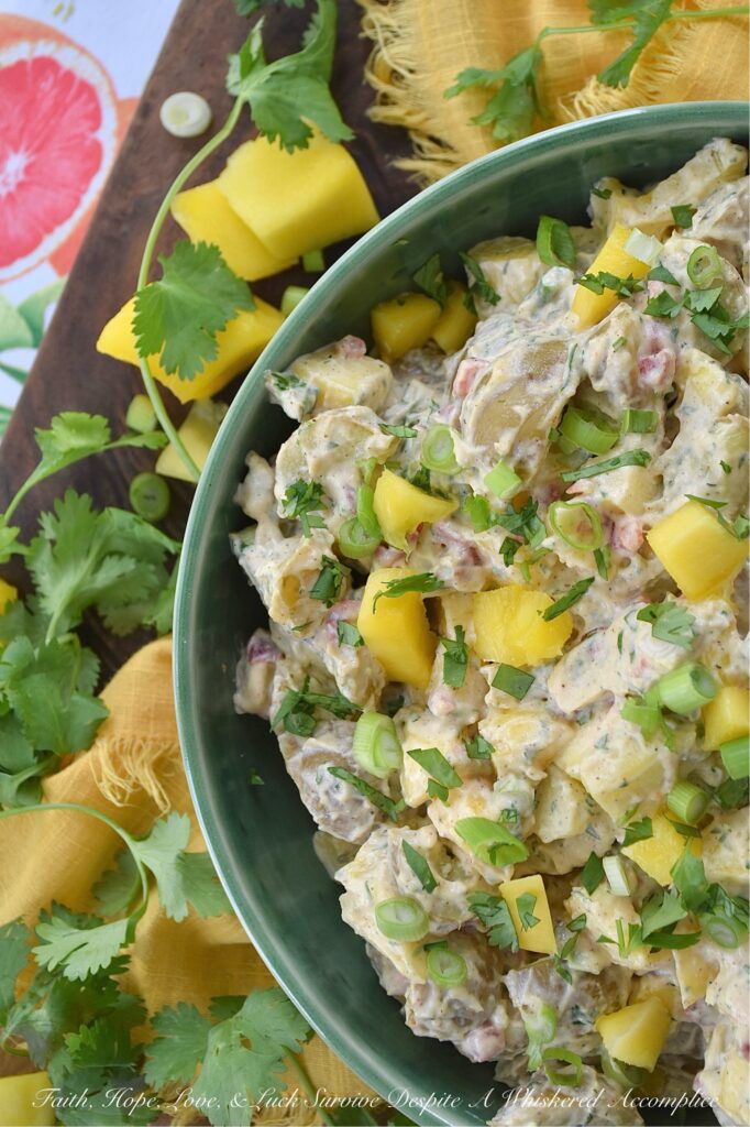 Creamy Cilantro Herb Caribbean Potato Salad - Tired of the same boring traditional potato salad? Bring a little tropical flavor to your next picnic or barbecue with this creamy Caribbean version, featuring jerk seasoning, diced pimentos, and fresh mango. This flavorful herby potato salad has a touch of heat and is just a little bit sweet. With cilantro, scallions, and a splash of vinegar to brighten things up, this island-inspired recipe turns a bag of small yellow potatoes into a side dish that will have everyone practically begging you for the recipe.
